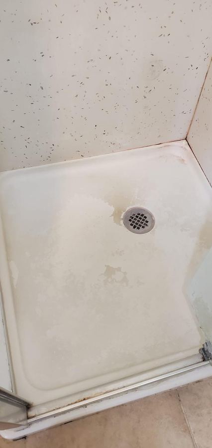 Shower pan before cleaning, discolored with soap scum and hard water buildup